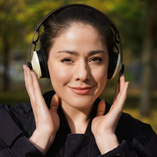 young woman in her 20s listening to music with cordless over-ear headphones outside in nature on a sunny day