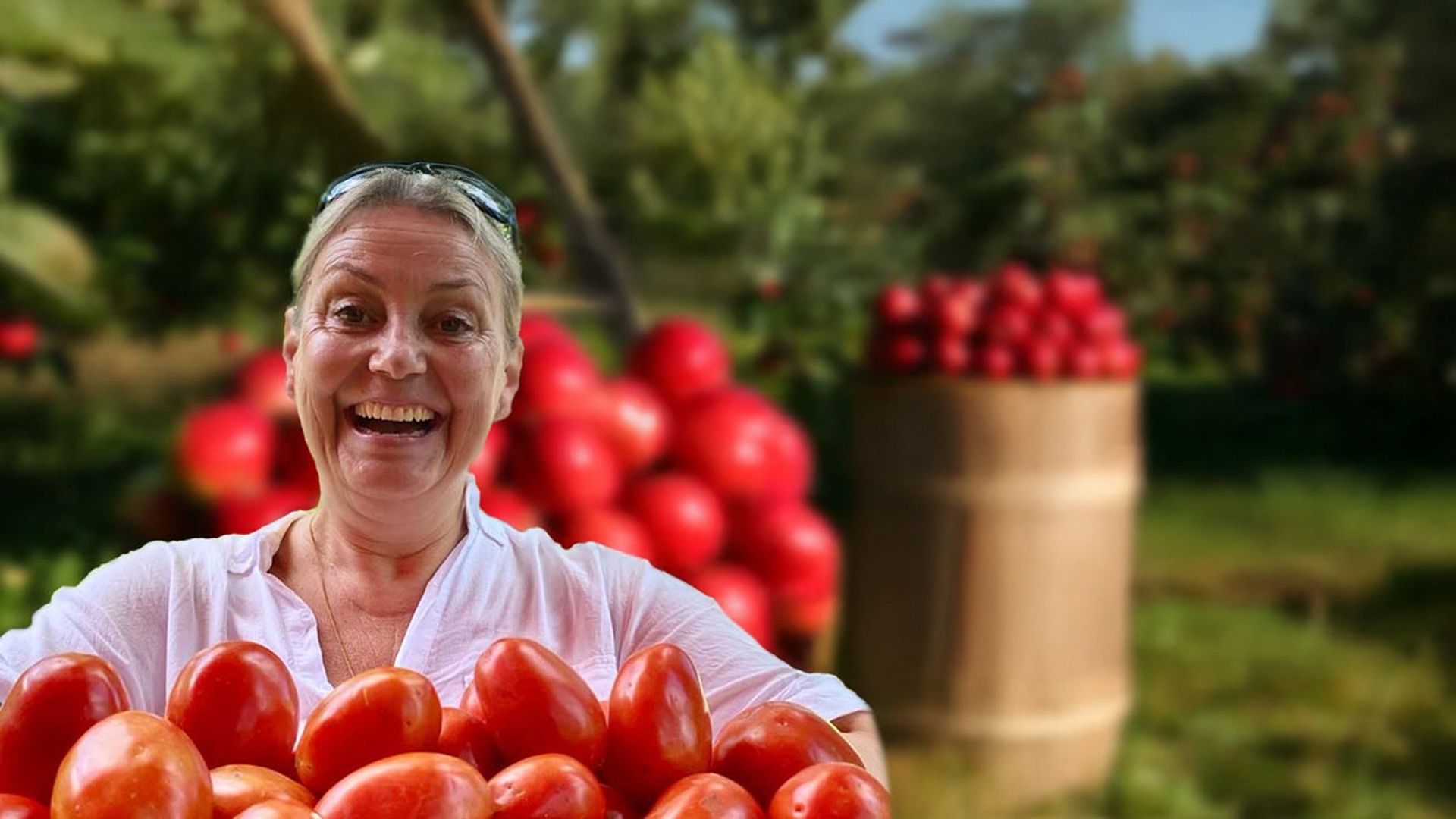 Agri-Homöopathie Camilla Sherr mit Tomaten in den Armen im Hintergrund Tomaten Ernte und grüne Bäume