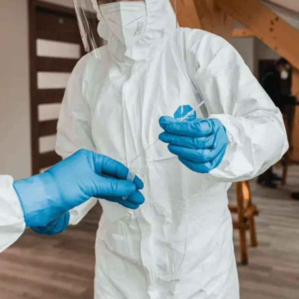 Person im weißen Schutzanzug mit Teströhrchen
