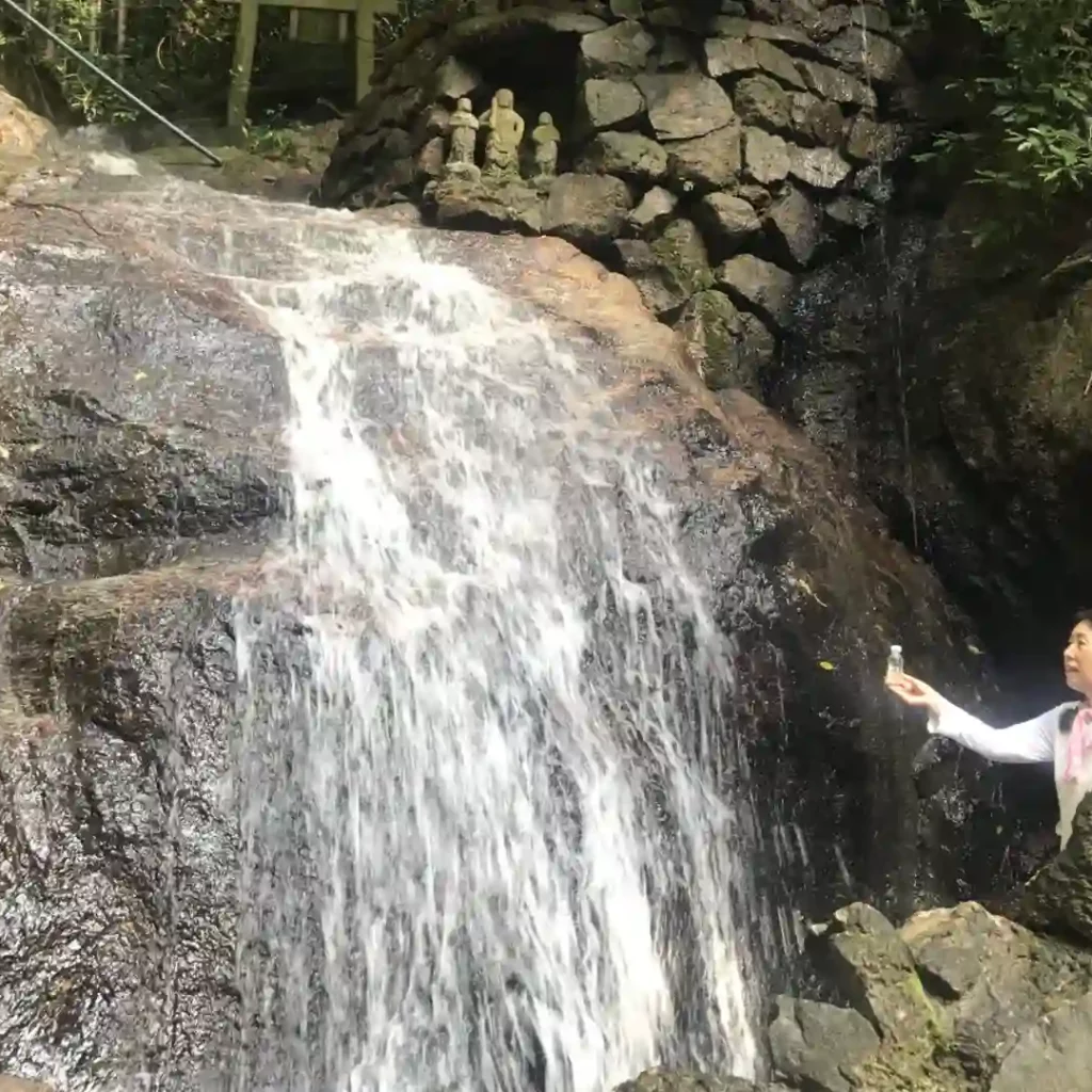 Sonnenschmidt_Krisen meistern – Wasserfall Frau mit Fläschchen an einem Wasserfall